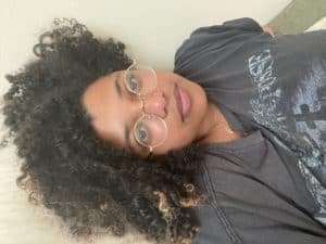 Headshot of medium black skinned astrologer with round, wire rimmed glasses and natural textured hair
